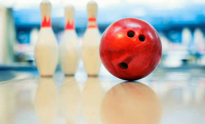 A red bowling ball and three white pins sit on a clean bowling lane.