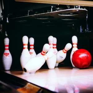 Ten bowling pins being pummeled by a red bowling ball.