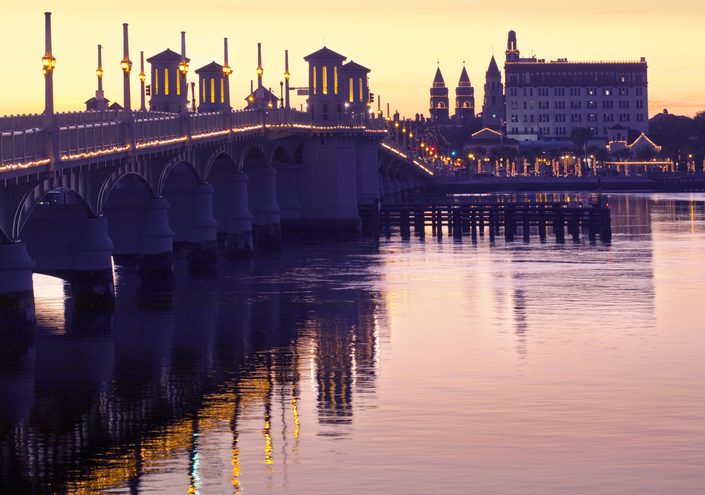 The Bridge of Lions illuminated tower piers stand over the Matanzas River between downtown Saint Augustine, Florida. The twin towers of Flagler College, the Cathedral Bascilica, and Saint Augustine's First National Bank identify the city's skyline. The bridge is listed on the National Register of Historic Places.