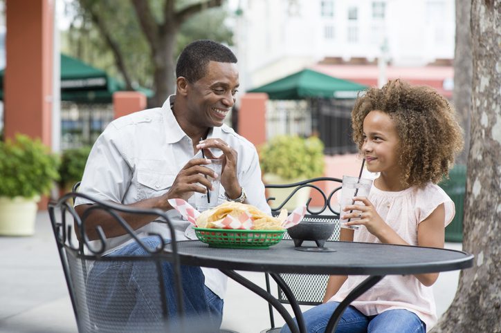 Father and daughter eating at outdoor restaurant table